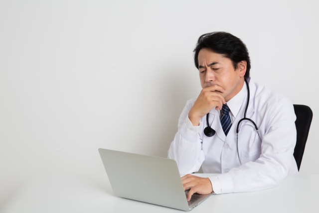 悩みながらPCを開く男性医師